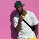 A photo shwoing Marlon Wayans sporting a white shirt and yellow pant, while leaning against a pink color wall.