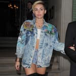 Miley Cyrus leaves her hotel arm in arm with her bodyguard The singer was wearing a white crop top black knee high boots denim hot pants and a matching denim jacket