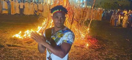 A photo showing Biniyam Shibre dressed in a traditional attire, around a bonfire.