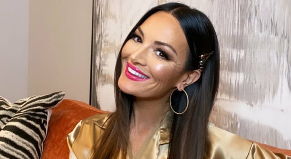 Lisa Barlow smiles while sitting on a couch during an interview