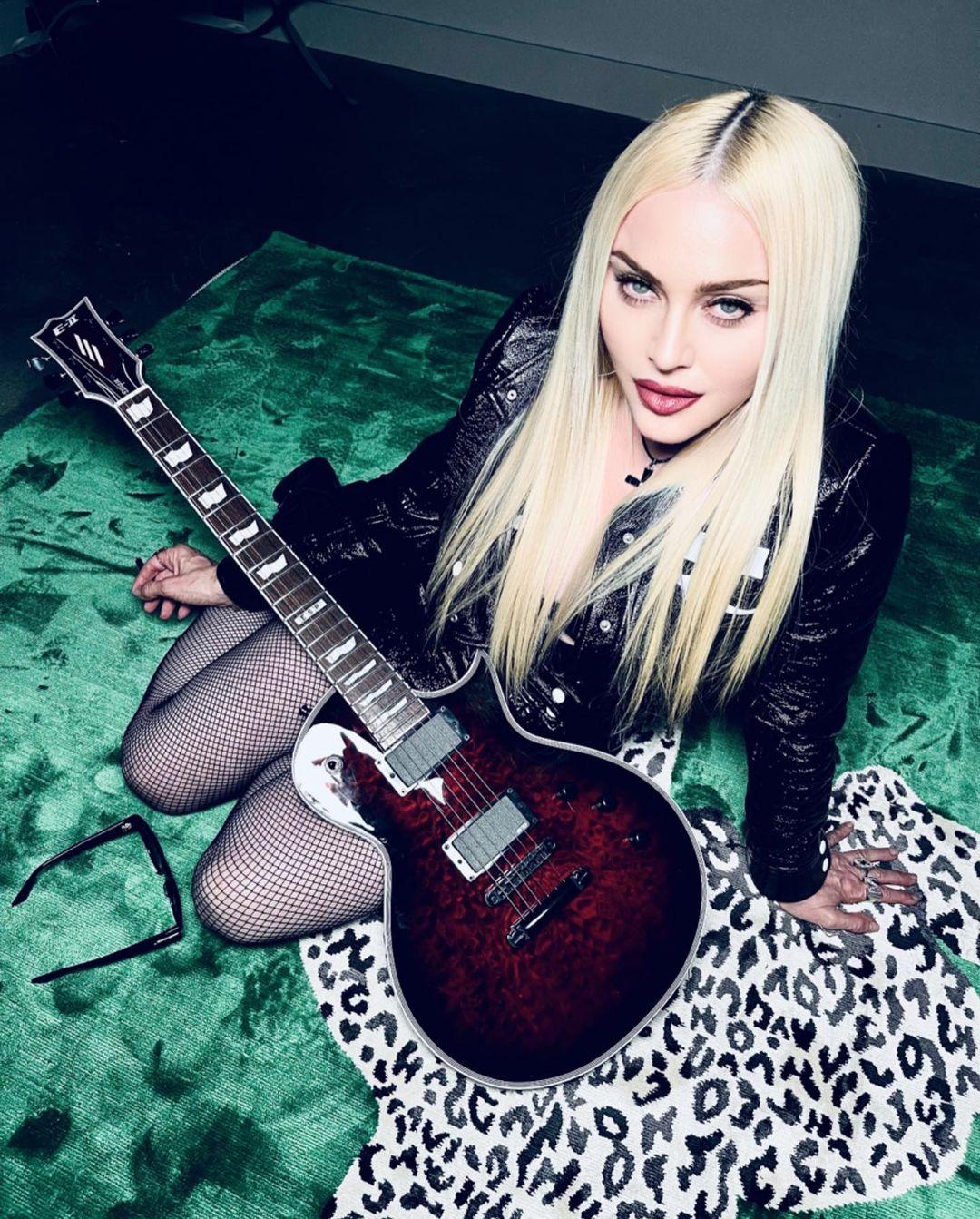 A photo of Madonna sitting with a guitar on her thighs.