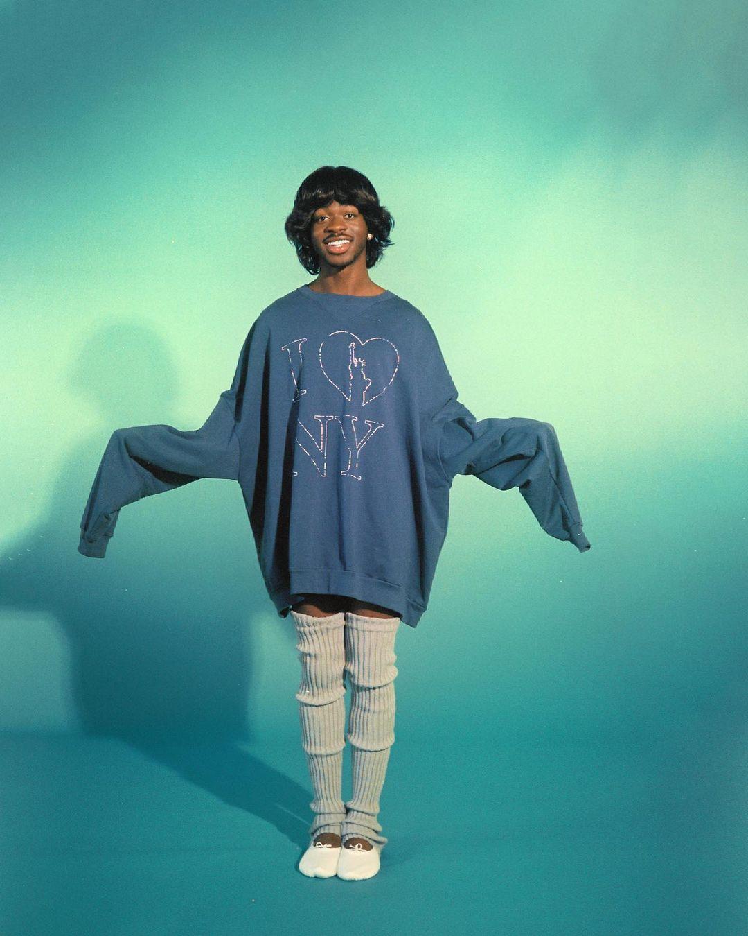 A photo showing Lil Nas X in an over-sized sweater and prop socks.