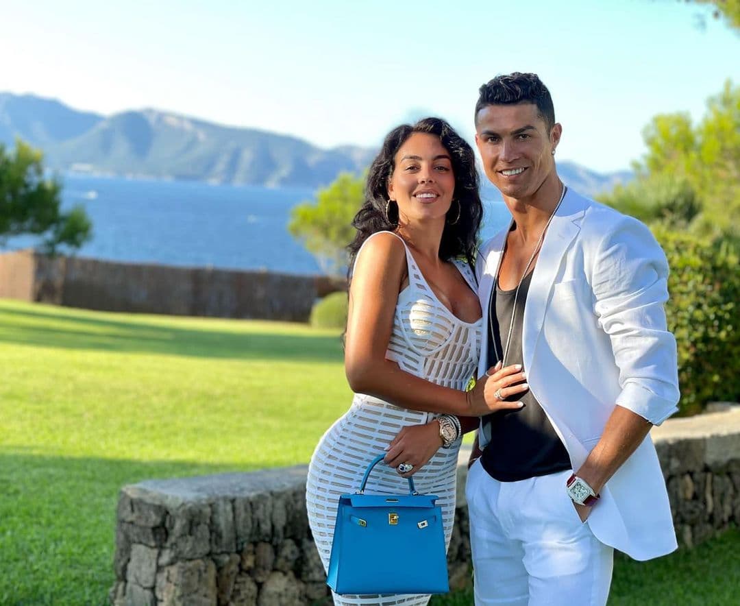 Couple posing together outdoors with mountains and blue water visible in the background