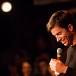 A photo showing John Mulaney telling jokes to a vast audience