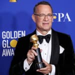 Tom Hanks holding a Golden Globes Award with a huge smile on his face.