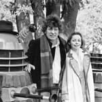Tom Baker poses as the Fourth Doctor in Doctor Who next to a Dalek and Sarah Baker