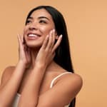 A tan woman smiling on a beige background.
