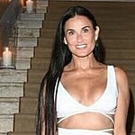 A photo showing Demi Moore at the edge of a staircase, sporting a white dress.