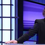 A lovely photo of Mayim Bialik in a black suit and purple inner blouse.