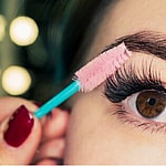 A woman applying mascara to her lashes.