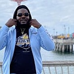 Ronald Ollie in a blue tracksuit in front of a beach.