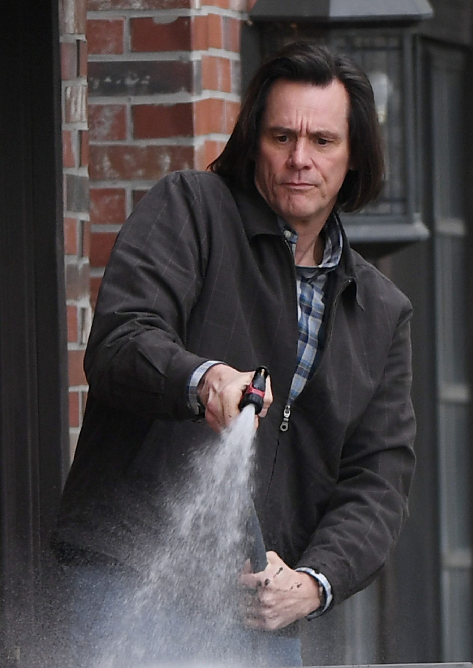 Jim Carrey sprays water out of a garden hose while watering the plants on set of a new movie