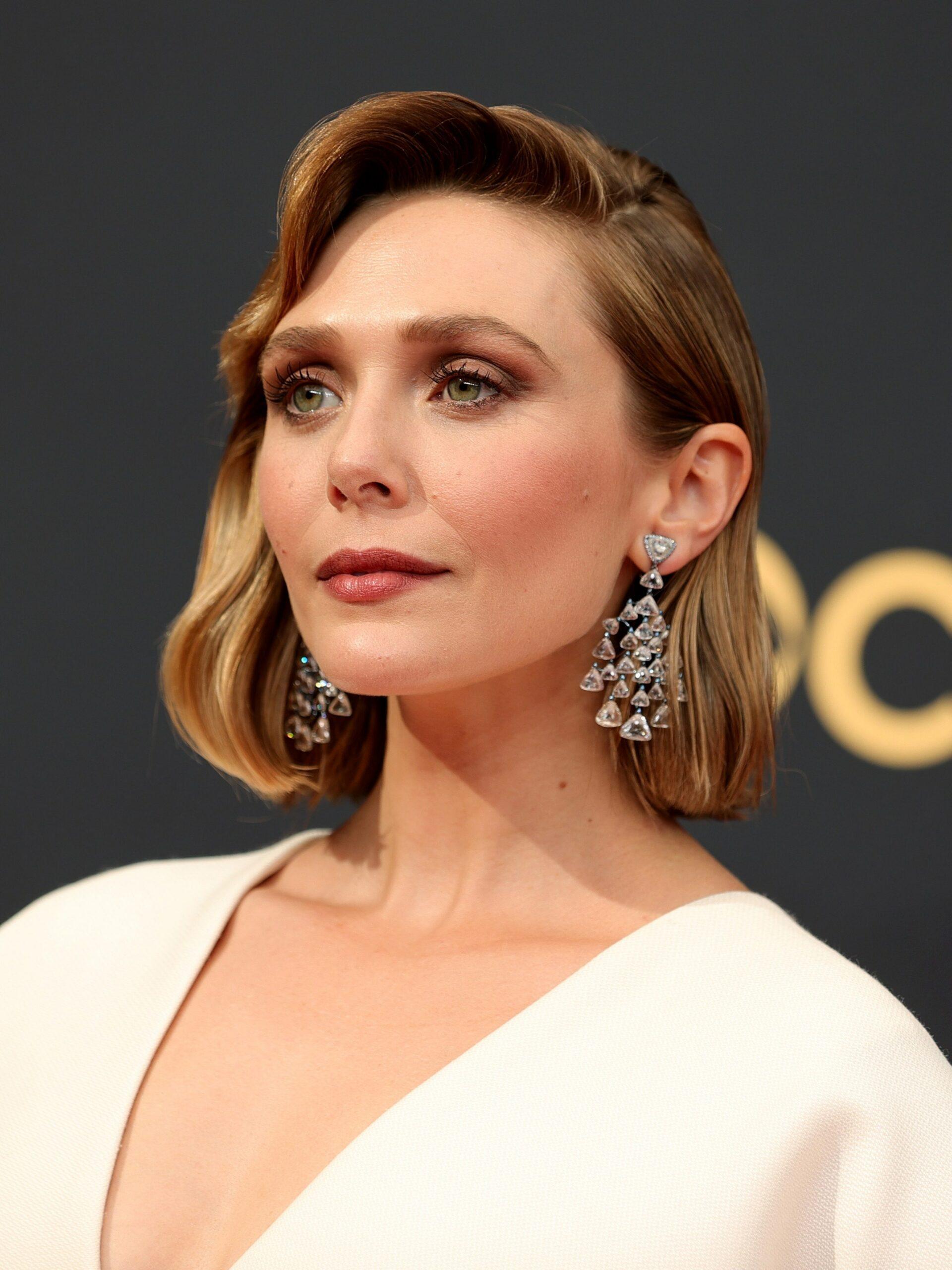 Elizabeth Olsen at an event wearing a cream-colored top and diamond earrings