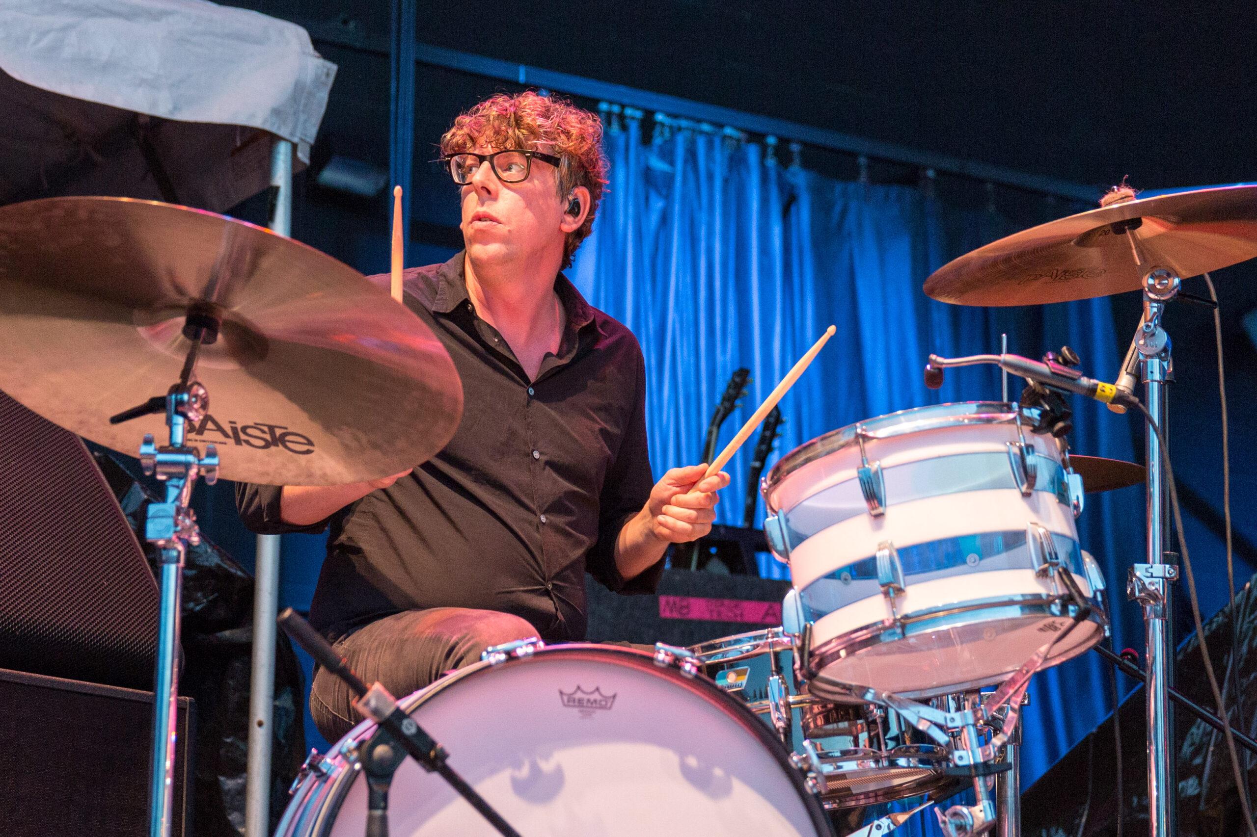 Drummer performing on stage with blue curtain backdrop