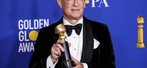Tom Hanks holding a Golden Globes Award with a huge smile on his face.