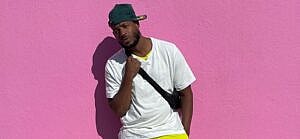 A photo shwoing Marlon Wayans sporting a white shirt and yellow pant, while leaning against a pink color wall.