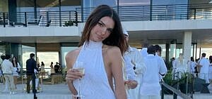 A photo showing Emily Ratajkowski in a white dress holding a glass of champagne