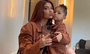 Woman in brown outfit holding child while taking mirror selfie