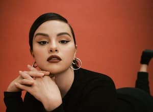 Selena Gomez laying down in front of a brown-red background.