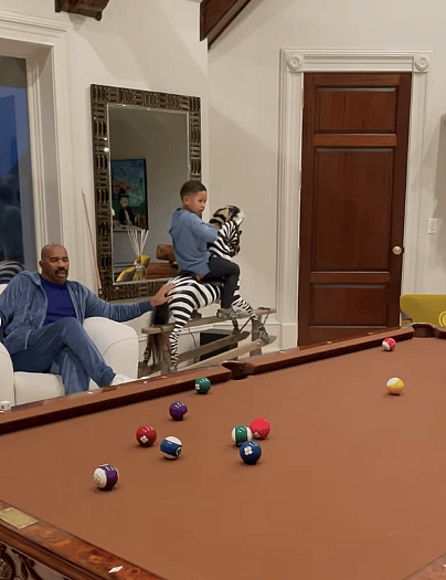 Steve Harvey pushing grandkid's rocking zebra.