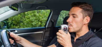 Man in car using breathalyzer.