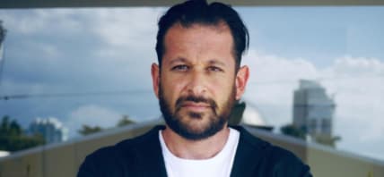 Man with dark hair wearing white tee shirt and black sweater.