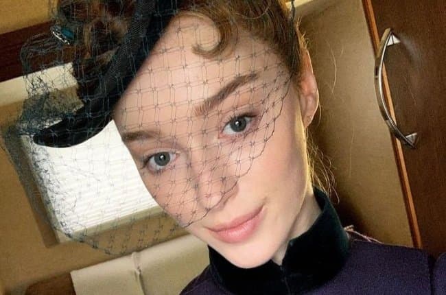 Phoebe Dynevor wearing a black turtleneck and mesh veil headpiece