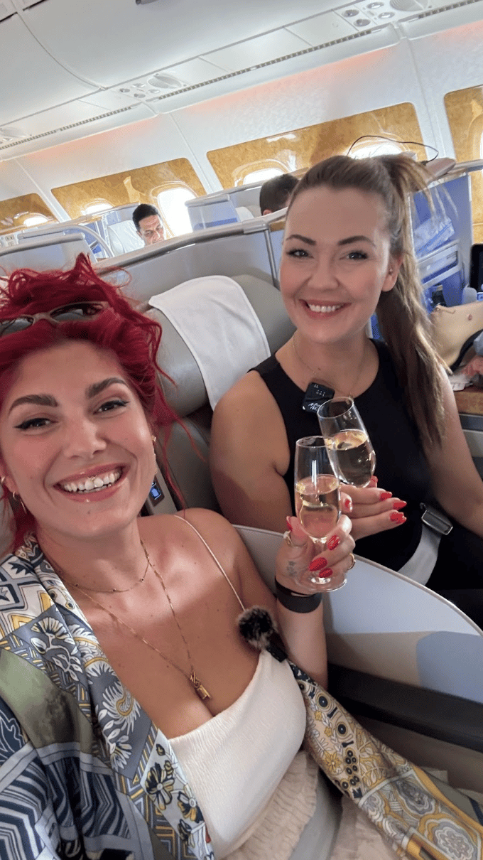 Two women on an airplane holding glasses of champaign.