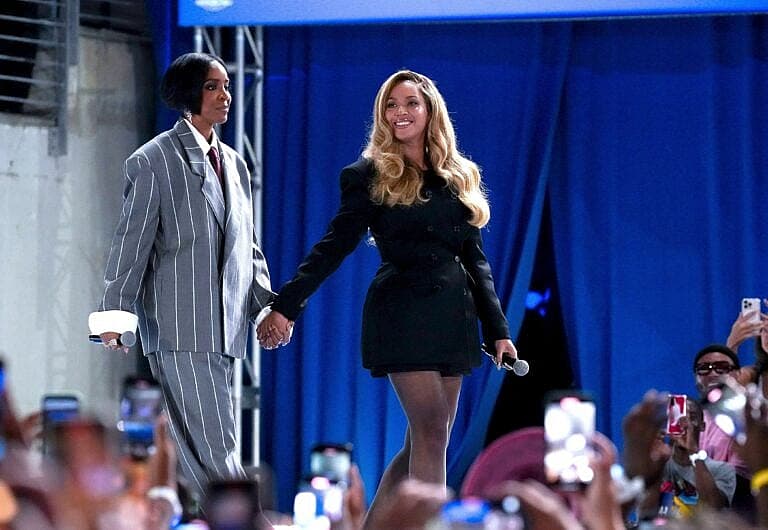 Two people holding hands on stage before a crowd with blue backdrop
