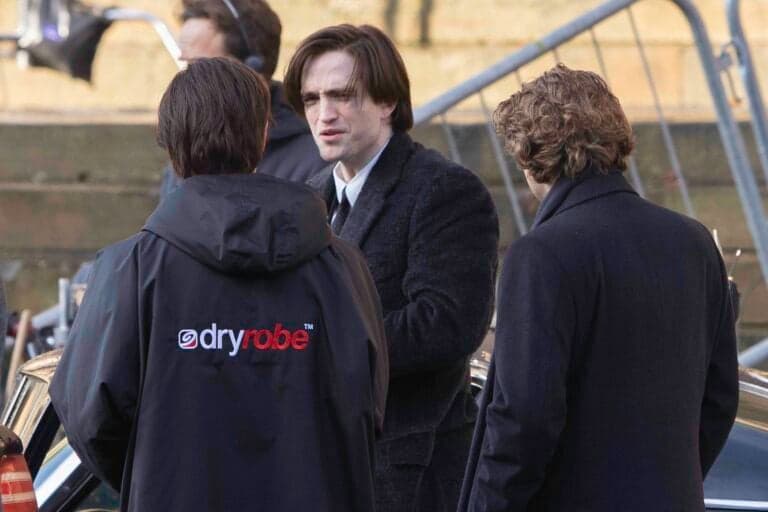 Robert Pattinson speaks with crew members on a film set