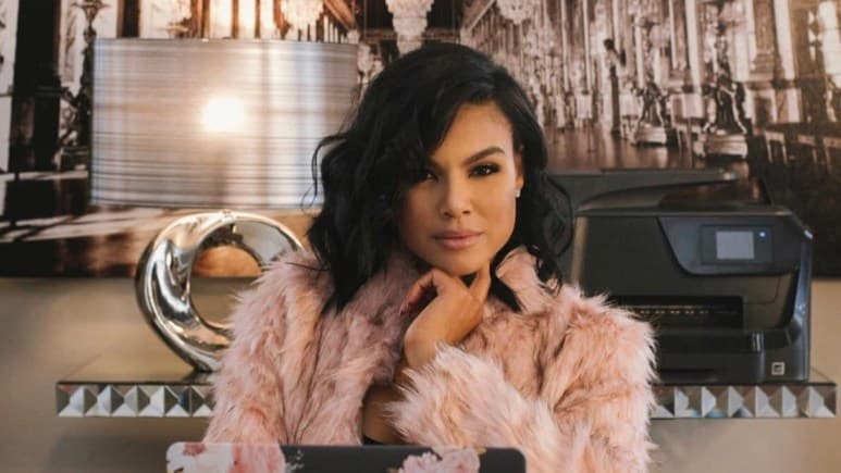 Mia Thornton sits at a desk wearing a pink fuzzy jacket in a studio setting.