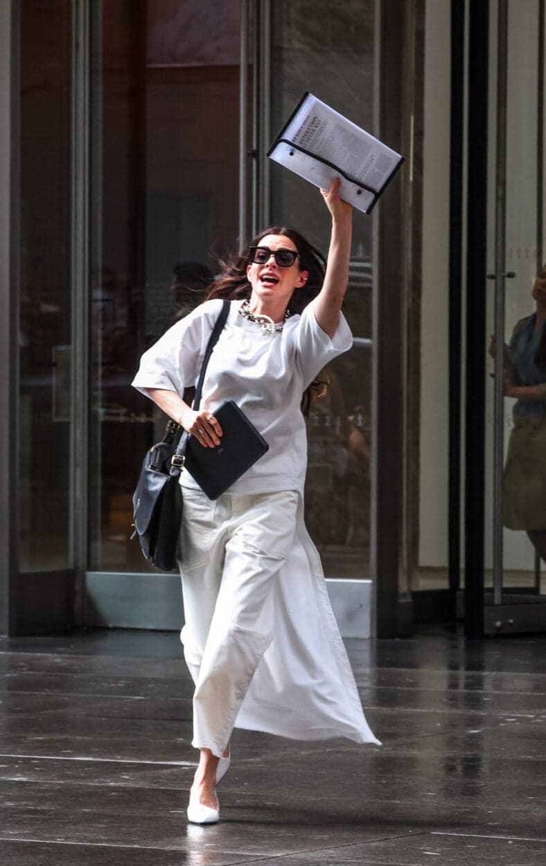 Anne Hathaway is seen running out of an office building waving a news article in the air as she films scenes for The Devil Wears Prada 2 this morning in New York City