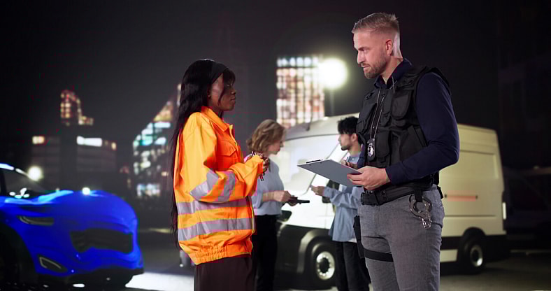 Homem conversando com uma mulher de colete laranja na beira da estrada.