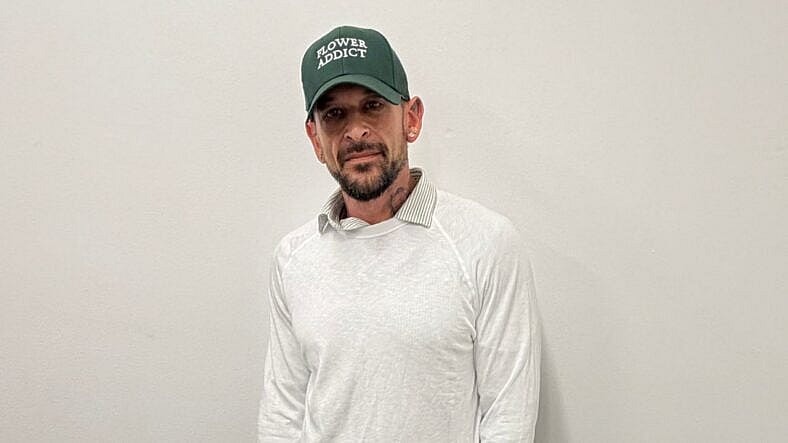 Homem de boné de beisebol verde e suéter branco.