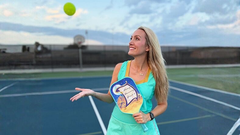Woman on a pickleball court, catching a ball.