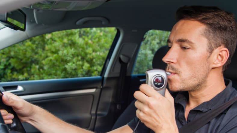 Man in car using breathalyzer.