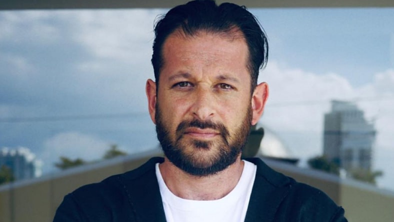 Man with dark hair wearing white tee shirt and black sweater.