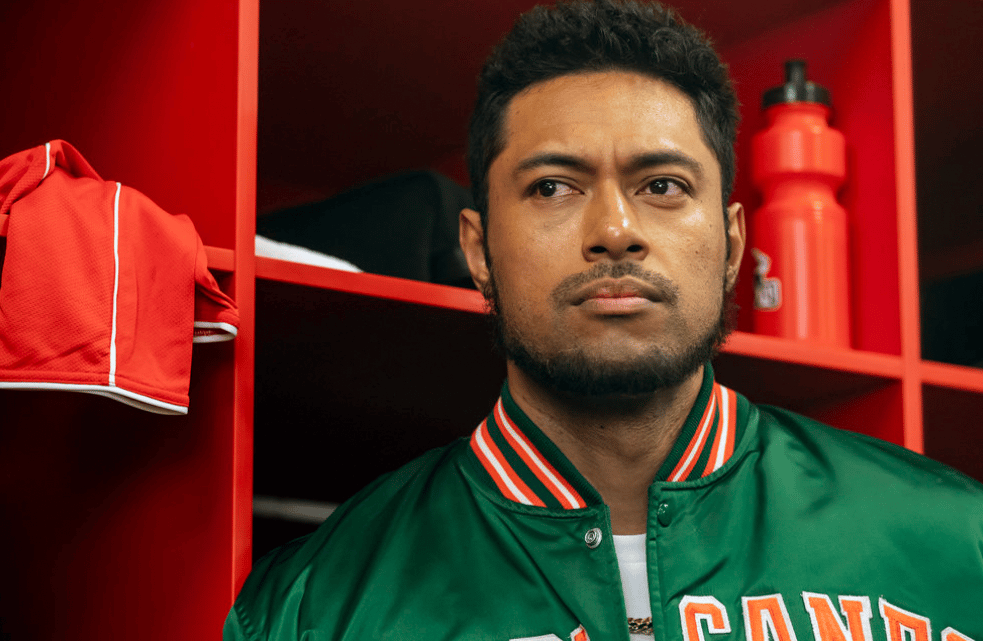 Man in green jacket with striped collar sitting in front of red locker room shelving
