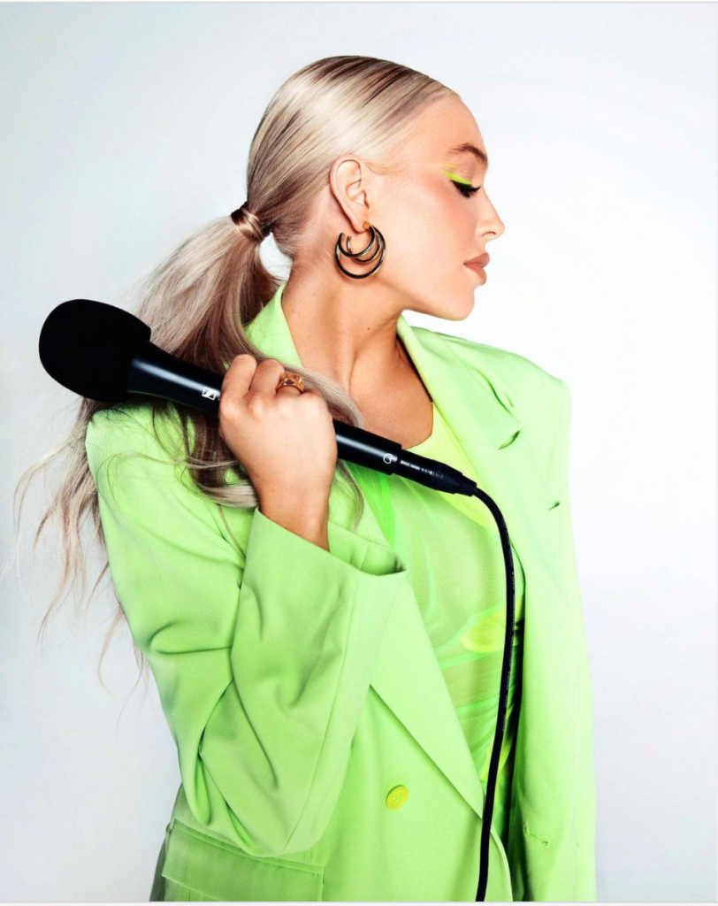 Alex Cooper in a green suit with a microphone
