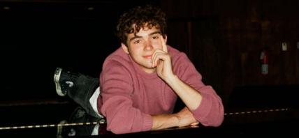 Joshua Bassett laying on top of a piano