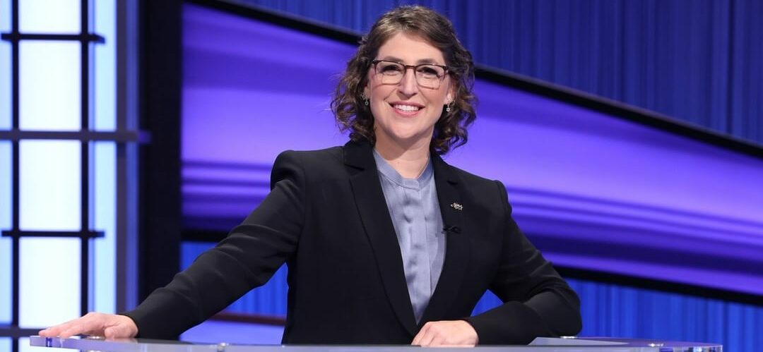 A lovely photo of Mayim Bialik in a black suit and purple inner blouse.