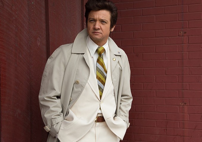 A photo of Jeremy Renner in a creme color outfit, with a striped tie.