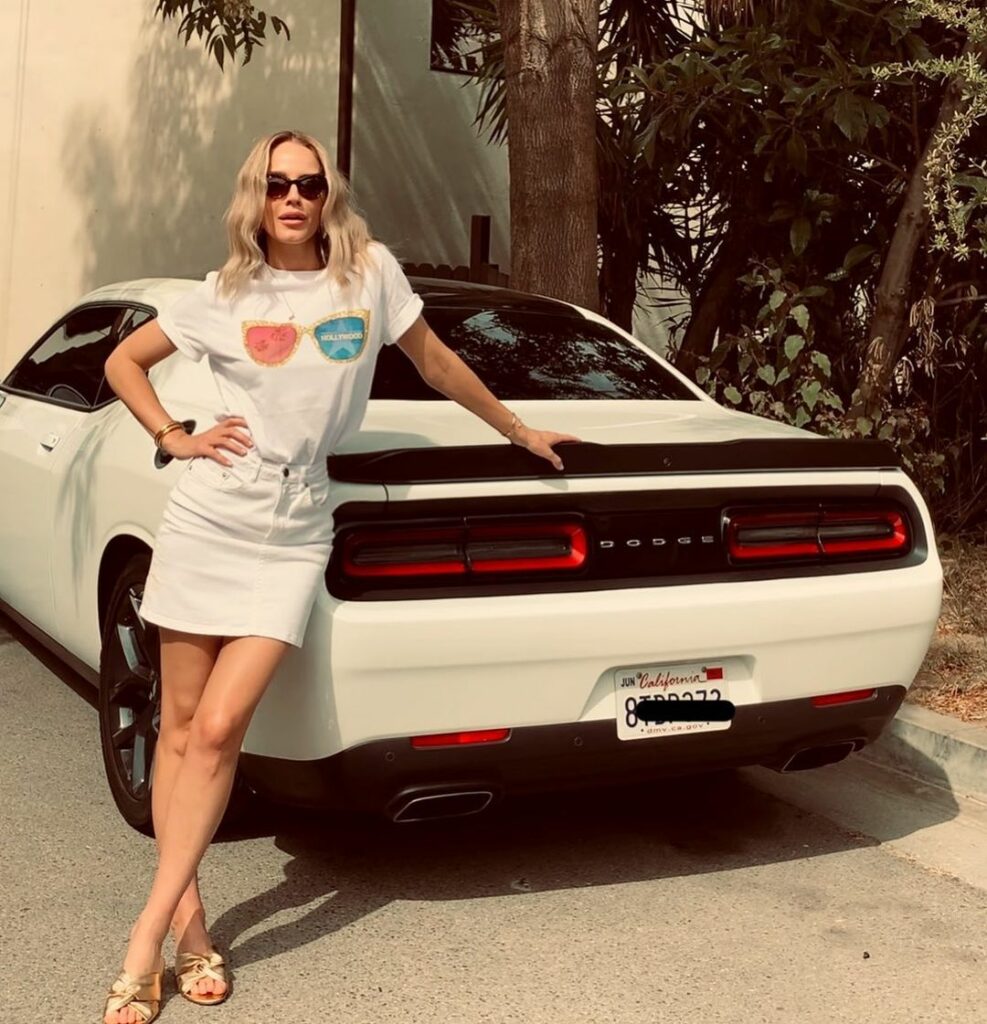 A photo showing Monet Mazur in a skimpy white dress beside a stylish car.