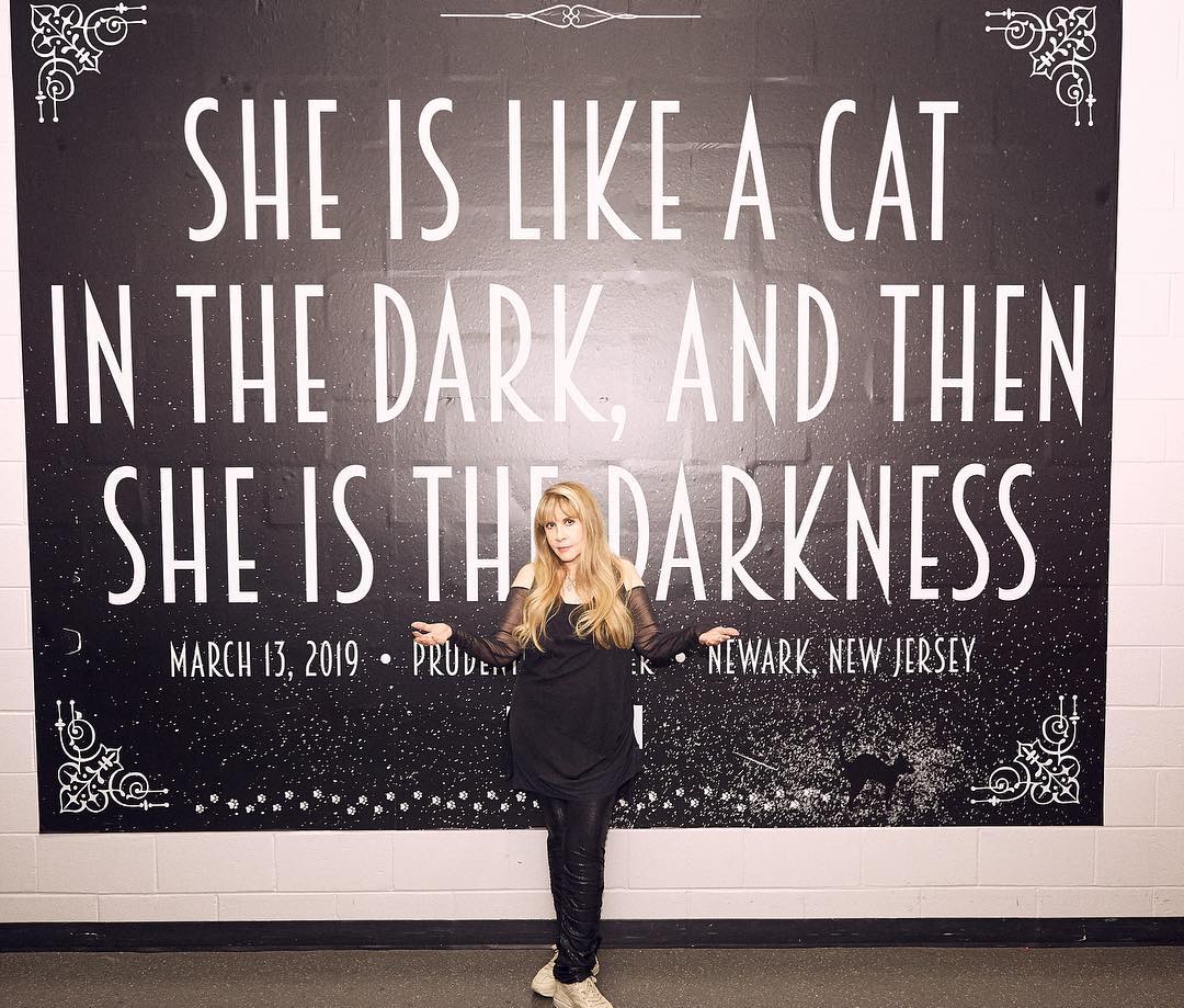 A photo of Stevie Hicks in a black long-sleeve blouse and pant, posing in front of a mantra