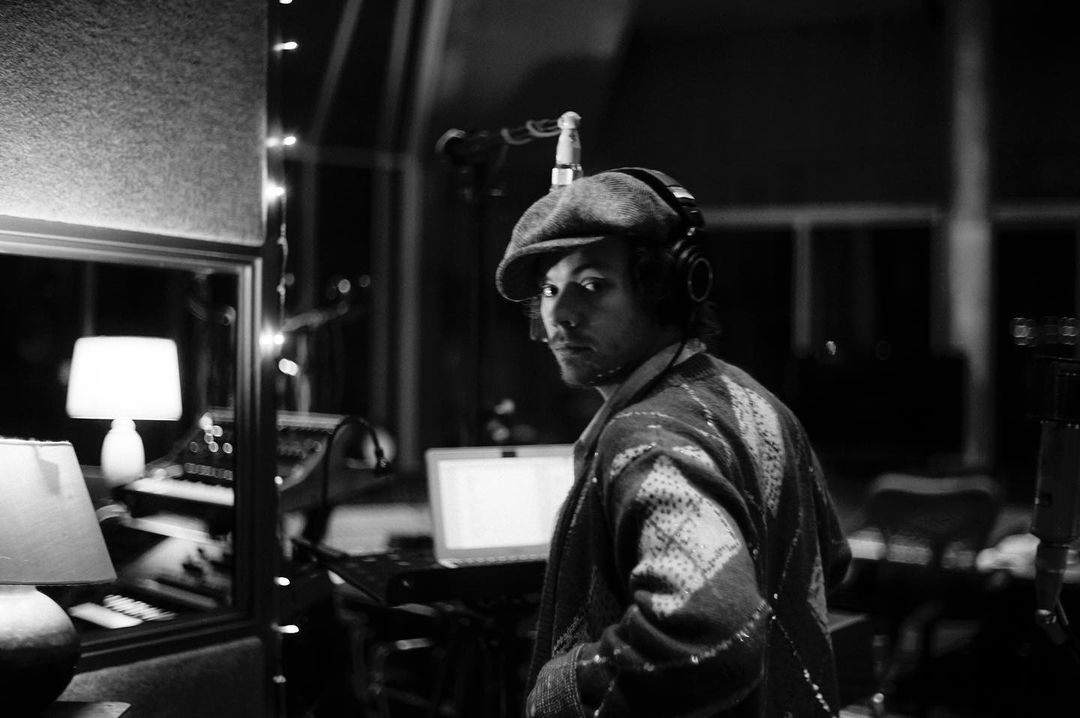 A black and white themed photo showing Harry Styles in a room with equipments.