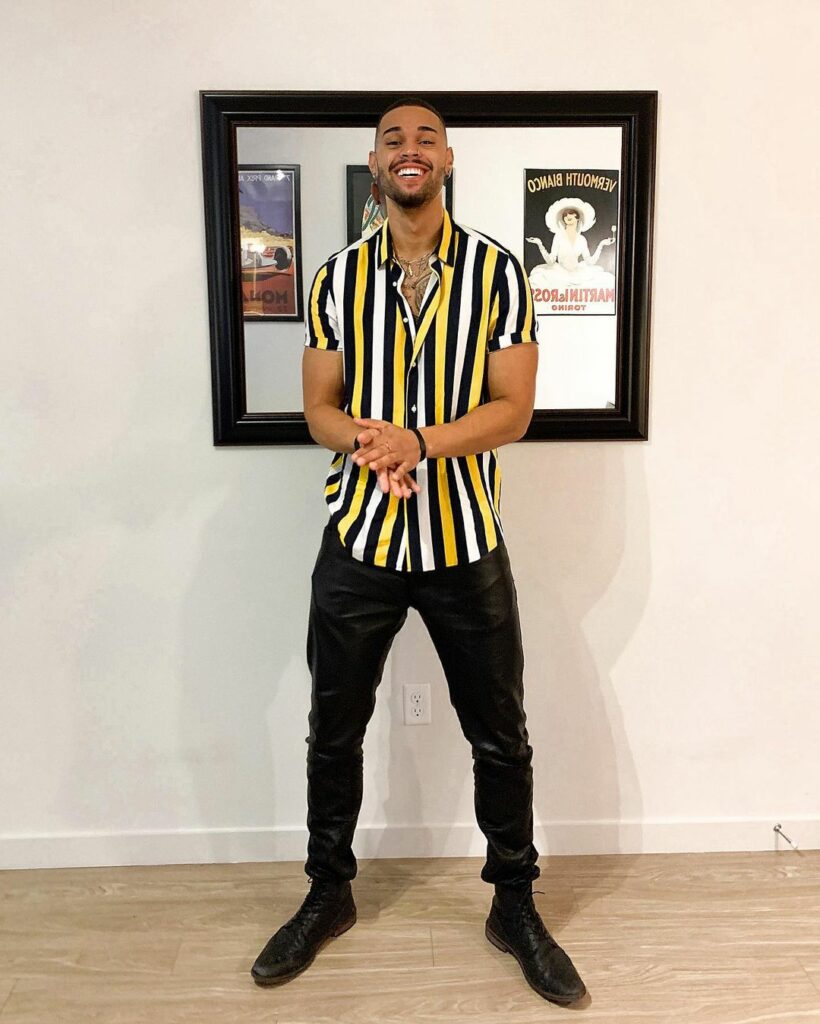 A photo of Nayte Olukoya porting a white and yellow striped short-sleeve shirt and black pant.