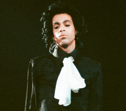 Prince in a black long-sleeve T-shirt with a white scarf around his neck.