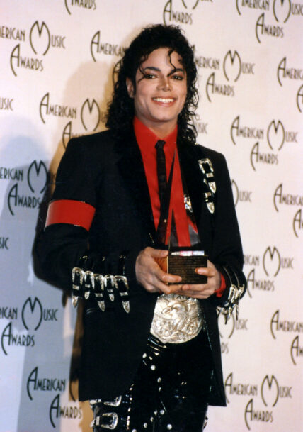 A photo showing Michael Jackson in his signature black suit paired with a red inner T-shirt at an event.