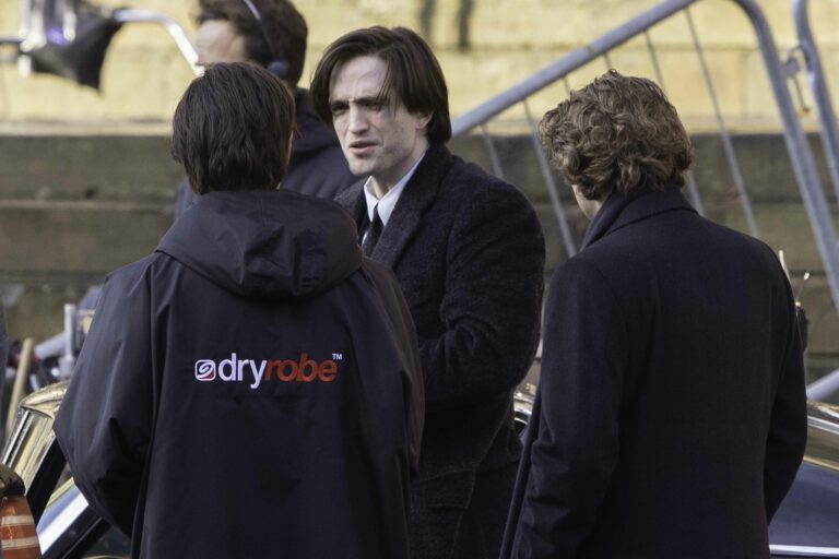 Robert Pattinson speaks with crew members on a film set