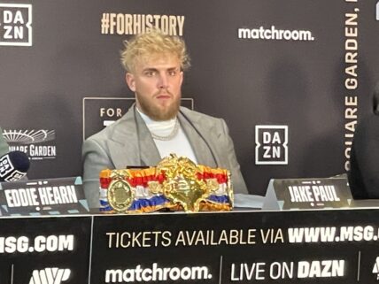 Jake Paul looks out at the media as he promotes the Taylor vs Serrano boxing event as his girlfriend sits in crowd nearby in NYC
